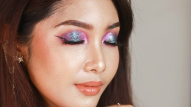 Profesyonel makyajlı, parlak tenli ve koyu renk saçlı güzel bir Asyalı kız. Renkli dumanlı gözler.