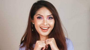 Beyaz arka planda renkli makyajlı güzel bir Asyalı kız çerçeveye bakar..