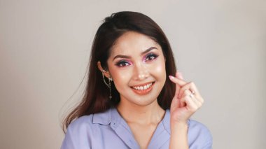 Hoş, koyu renk saçlı, nazik gülüşlü bir kadın Koreli bir aşk işareti yapar. Minik kalp hareketi. Vücut dili kavramı