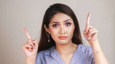 Güzel Asyalı genç bir kadının portresi beyaz arkaplanda izole edilmiş fotokopi alanını karıştırır ve parmaklarını yukarı doğru gösterir.