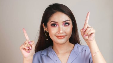 Güzel Asyalı genç bir kadının portresi gülümsüyor ve beyaz arka planda izole edilmiş fotokopi alanını işaret ediyor.