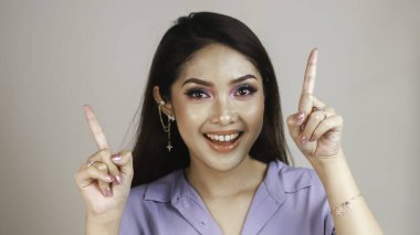 Güzel Asyalı genç bir kadının portresi gülümsüyor ve beyaz arka planda izole edilmiş fotokopi alanını işaret ediyor.