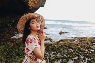 Plaj şapkası takan genç bir Asyalı kız Gunungkidul, Endonezya 'daki mavi gökyüzü kumsalında dinleniyor.
