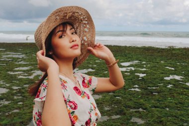 Plaj şapkası takan genç bir Asyalı kız Gunungkidul, Endonezya 'daki mavi gökyüzü kumsalında dinleniyor.