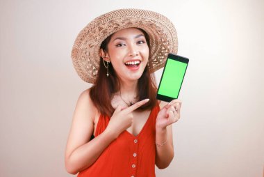 Heyecanlı ve gülümseyen Asyalı genç kadın elinde akıllı telefonuyla yeşil ekran gösteriyor.