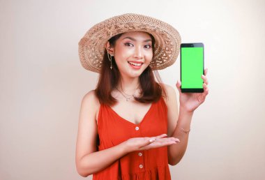 Heyecanlı ve gülümseyen Asyalı genç kadın elinde akıllı telefonuyla yeşil ekran gösteriyor.
