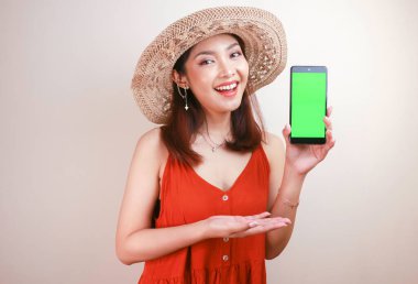 Heyecanlı ve gülümseyen Asyalı genç kadın elinde akıllı telefonuyla yeşil ekran gösteriyor.