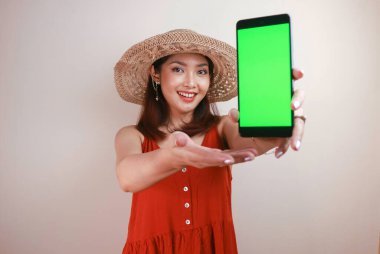 Heyecanlı ve gülümseyen Asyalı genç kadın elinde akıllı telefonuyla yeşil ekran gösteriyor.