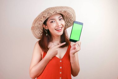 Heyecanlı ve gülümseyen Asyalı genç kadın elinde akıllı telefonuyla yeşil ekran gösteriyor.