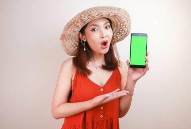 Heyecanlı ve şok olmuş Asyalı kadın elinde akıllı telefonuyla ekranı gösteriyor..