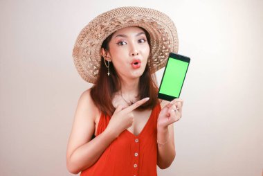 Heyecanlı ve şok olmuş Asyalı kadın elinde akıllı telefonuyla ekranı gösteriyor..