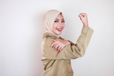 Kahverengi üniforma giyen, pazılarını gösteren ve gülümseyen muhteşem, güçlü, genç, Müslüman bir Asyalı kadın. Endonezyalı kız güçlü konsept.