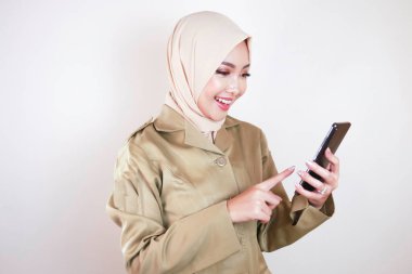 Gülümseyen devlet çalışanı akıllı telefondan boş ekran gösteriyor. Genç bir Asyalı Müslüman PNS haki rengi üniforma ve başörtüsü giyiyor..