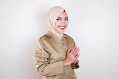 Müslüman sivil işçi kahverengi üniforma giyiyor ve tesettüre el hareketi yapıyor ve kameraya gülümsüyor.