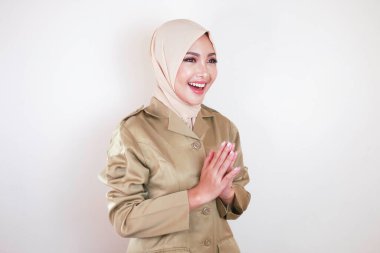 Müslüman sivil işçi kahverengi üniforma giyiyor ve tesettüre el hareketi yapıyor ve kameraya gülümsüyor.