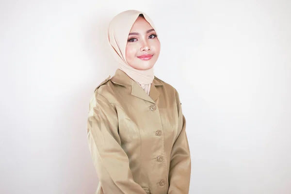 カメラには茶色の制服を着た若いアジア系ムスリム女性とヒジャーブの笑顔が描かれている インドネシア政府職員の制服 — ストック写真