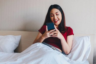 Genç ve güzel bir Asyalı kadın, akıllı telefonunu tutarken gülümsüyor..