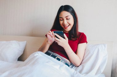 Genç ve güzel bir Asyalı kadın, akıllı telefonunu tutarken gülümsüyor..