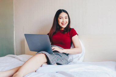 Evde dizüstü bilgisayarla çalışırken gülümseyen Asyalı genç bir iş kadını. İçerideki dizüstü bilgisayara bakan pozitif iş kadınının portresi