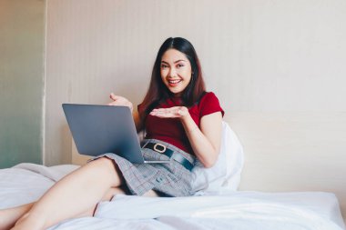 Evde dizüstü bilgisayarla çalışırken gülümseyen Asyalı genç bir iş kadını. İçerideki dizüstü bilgisayara bakan pozitif iş kadınının portresi