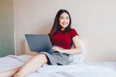 Evde dizüstü bilgisayarla çalışırken gülümseyen Asyalı genç bir iş kadını. İçerideki dizüstü bilgisayara bakan pozitif iş kadınının portresi