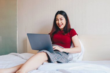 Evde dizüstü bilgisayarla çalışırken gülümseyen Asyalı genç bir iş kadını. İçerideki dizüstü bilgisayara bakan pozitif iş kadınının portresi