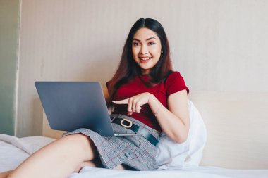 Evde dizüstü bilgisayarla çalışırken gülümseyen Asyalı genç bir iş kadını. İçerideki dizüstü bilgisayara bakan pozitif iş kadınının portresi