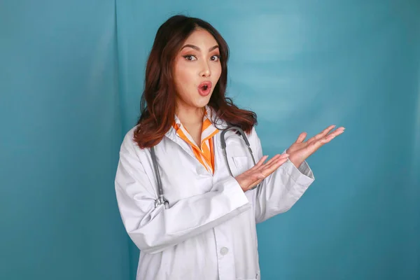 一位年轻的亚洲女医生的画像 令医学专业人员震惊 并指向一个蓝色背景的复制空间 — 图库照片