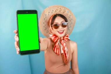 Genç Asyalı mutlu bir kadının telefonunda mavi bir arka planla izole edilmiş fotokopi alanı göstermesi.