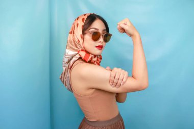 Genç Asyalı güçlü bir kadının kaslarını göstermesi kavramı mavi bir arka planda izole edilmiş.