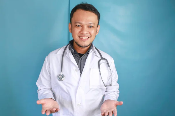 Young male doctor presenting an idea while looking smiling on isolated blue background