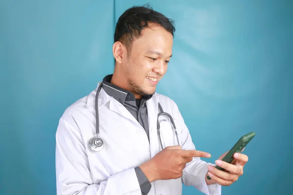 年轻的亚洲男医生笑着指着他的智能手机 — 图库照片