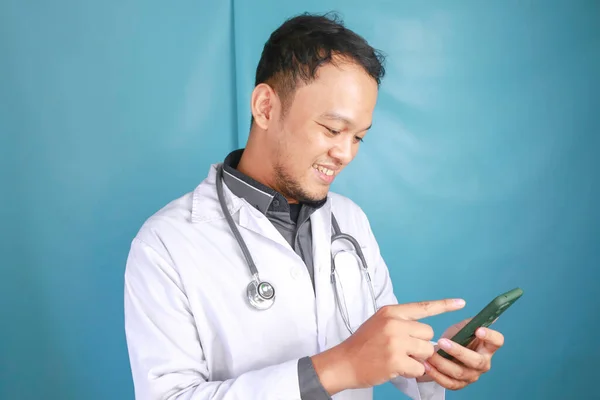年轻的亚洲男医生笑着指着他的智能手机 — 图库照片