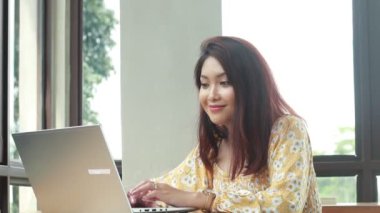 young asian woman working with laptop computer and looking at camera