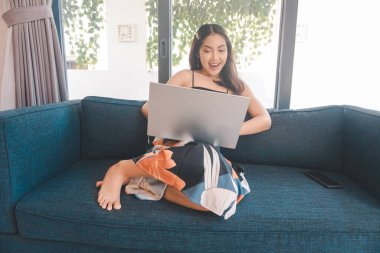 Genç Asyalı kadın zamanını evde oturup gülümseyerek ve dizüstü bilgisayarıyla çalışarak geçiriyor..