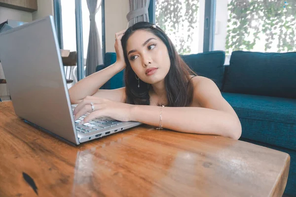 Genç Asyalı kadın zamanını evde oturup hayal kırıklığına uğramış ve yorgun bir şekilde dizüstü bilgisayarı üzerinde çalışarak geçiriyor..