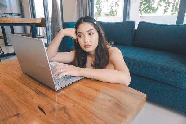 Genç Asyalı kadın zamanını evde oturup hayal kırıklığına uğramış ve yorgun bir şekilde dizüstü bilgisayarı üzerinde çalışarak geçiriyor..