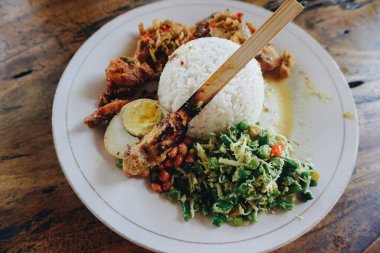 Nasi Kampı Ayam Betutu. Cassava yapraklarıyla doldurulmuş balili kızarmış tavuk. Yanında pilav, Sate Lilit, Jukut Antungan, Lawar Nangka ve Sambal Matah var..