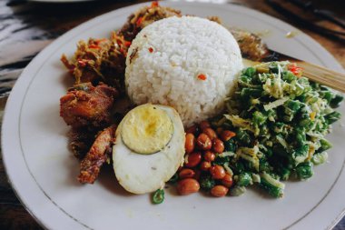 Nasi Kampı Ayam Betutu. Cassava yapraklarıyla doldurulmuş balili kızarmış tavuk. Yanında pilav, Sate Lilit, Jukut Antungan, Lawar Nangka ve Sambal Matah var..