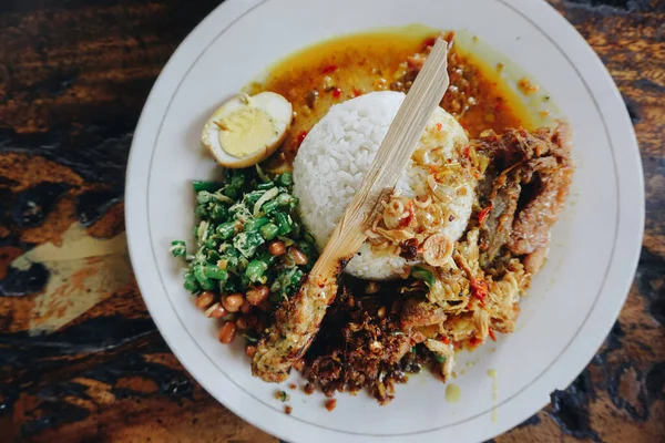 Nasi Kampı Ayam Betutu. Cassava yapraklarıyla doldurulmuş balili kızarmış tavuk. Yanında pilav, Sate Lilit, Jukut Antungan, Lawar Nangka ve Sambal Matah var..