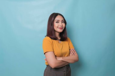Portrait of a confident smiling girl standing with arms folded and looking at camera isolated over blue background