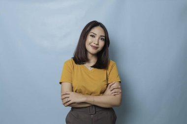 Portrait of a confident smiling girl standing with arms folded and looking at camera isolated over blue background