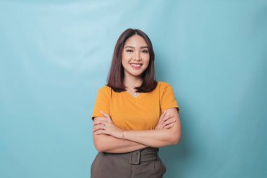 Portrait of a confident smiling girl standing with arms folded and looking at camera isolated over blue background
