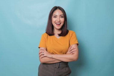 Portrait of a confident smiling girl standing with arms folded and looking at camera isolated over blue background