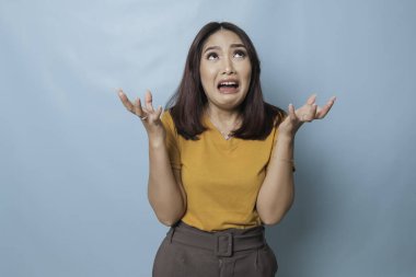 Beautiful young woman crying feeling very depressed isolated by blue background shouting loud