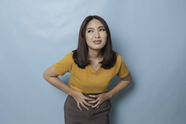 Young Asian woman with arms on stomach and bending over with stomachache expression
