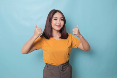 Young pretty woman smiling joyfully and looking happy, feeling carefree and positive with both thumbs up isolated by blue background