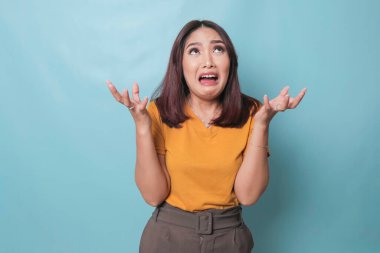 Beautiful young woman crying feeling very depressed isolated by blue background shouting loud