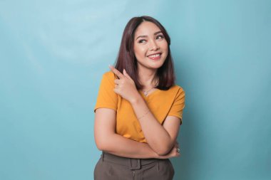 An excited young woman presenting and pointing upwards the copy space, isolated on blue background