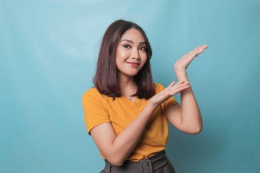 An excited young woman presenting and pointing upwards the copy space, isolated on blue background